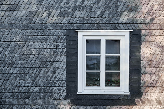 White casement window with mullions, fastened in a black building facade made of slate shingles