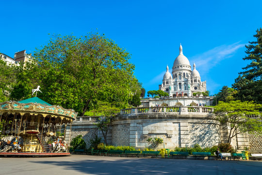 Sacre Coeur Basilica in Paris at day with blue bright sky and green grass and blooming trees.