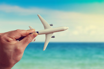 Human hand holding model airplane against the background of the sea landscape. The concept of summer vacation.