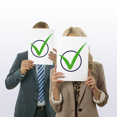 Ein Paar,  das sich ein Blatt Papier mit grünen Häkchen vor das Gesicht hält