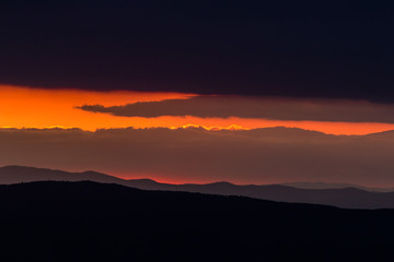A sunset framed between some dark mountains and clouds, creating an oblique stripe