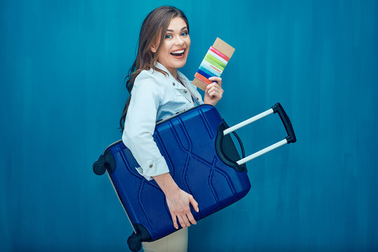 Smiling young woman holding suitcase, passport, ticket
