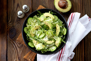 Organic healthy salad of iceberg, avocado and cucumber with olive oil and sesame seeds.