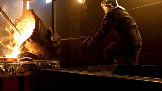 Worker controlling metal melting in furnaces. Workers operates at the metallurgical plant. The liquid metal is poured into molds.