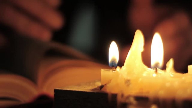 Monk reading and touching a yellow pages of old book. Close-up candle light.
