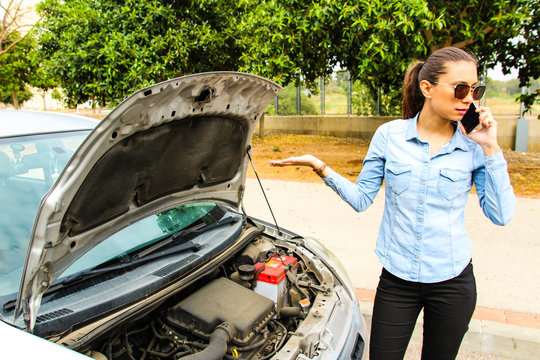 A woman with a broken car, talking on the phone and  waits for assistance