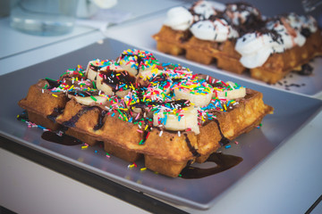 Close up of sweet waffles with banana, chocolate sauce and colorful decoration 