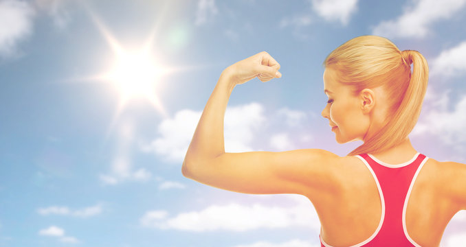 happy sporty woman showing biceps over sky and sun