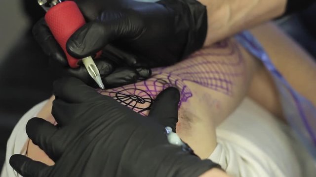 The tattoo artist makes a black tattoo on man shoulder