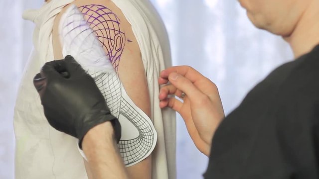 The tattoo artist translates the sketch of the tattoo onto the skin of the shoulder