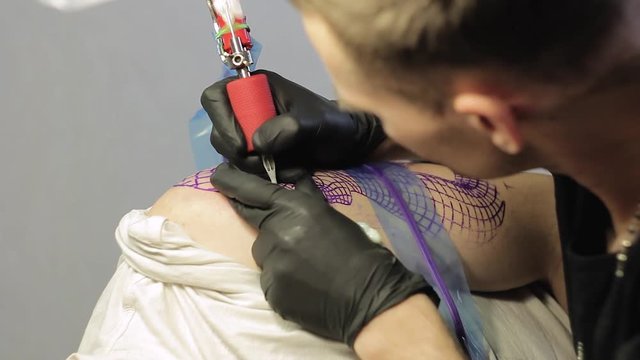 The tattoo artist makes a black tattoo on man shoulder