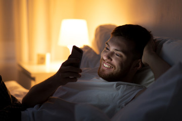 Fototapeta premium happy young man with smartphone in bed at night