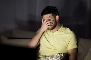 Obraz premium scared man watching tv and eating popcorn at night