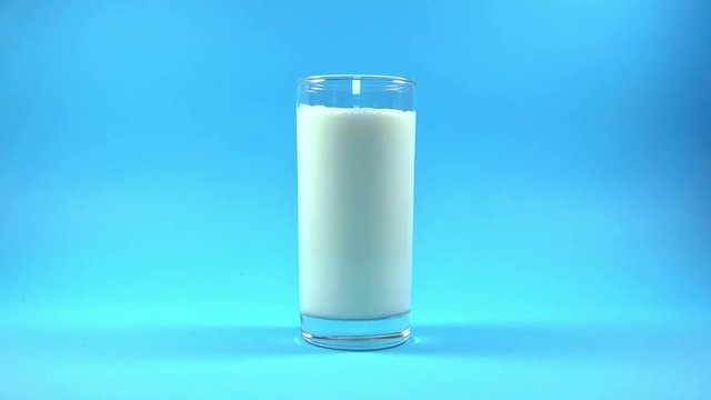 Glass of Milk with Pouring Splash on blue background. 4K