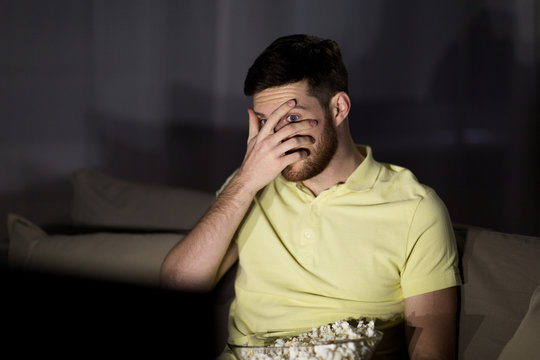 scared man watching tv and eating popcorn at night