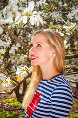 Portrait of spring blonde girl standing outdoor in blooming magnolia garden