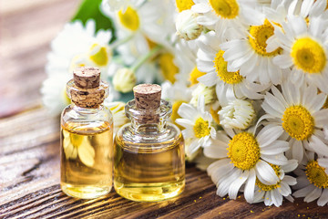 Essential oil in glass bottle with fresh chamomile flowers, beauty treatment. Spa concept. Selective focus. Fragrant oil of chamomile flowers, macro on wooden table horizontal.  - obrazy, fototapety, plakaty