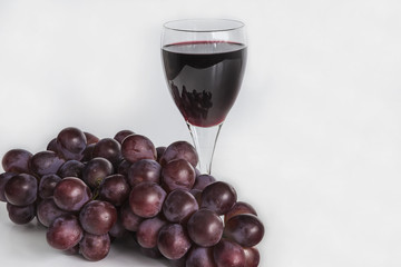 glass of red wine and red grapes on white background
