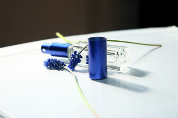 Open perfume, blue flowers and shell on white table close-up