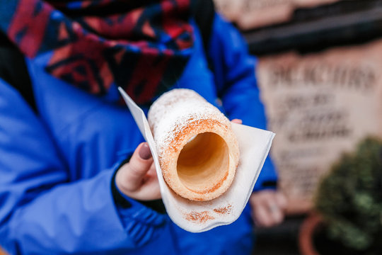 Woman hand closeup holding traditional czech sweet street food trdelnik On a background of cafe store