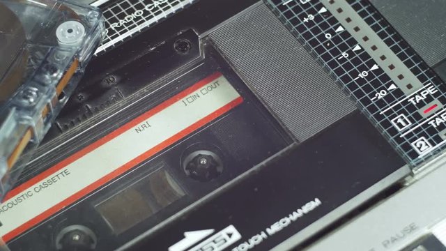 Playing an audio cassette in a tape recorder. Close-up. Black audio cassette with film rotates inside the deck. Red Record level indicator on a Vintage Cassette Deck.