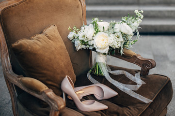 beautiful beige bridesmaid shoes with white bouquet lying on a brown easy chair
