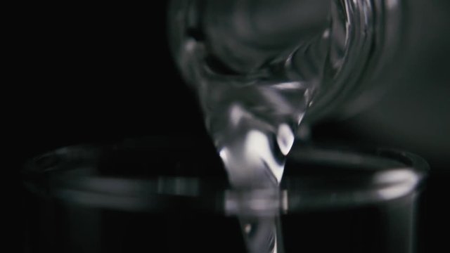 Vodka, water, clear liquid, drink pouring from the neck of a bottle, close-up, on a black background. Slow motion