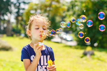 A little girl blowing soap bubbles in summer park. Background toninf for instagram filter.
