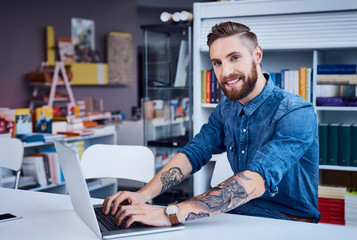 Happy designer, hipster working on laptop in office - obrazy, fototapety, plakaty