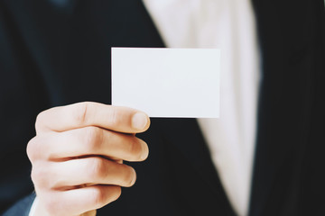 Closeup view of Businessman giving a empty white business card.Horizontal mockup, blurred background.