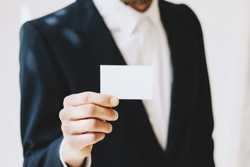 Fototapeta premium Businessman giving a blank white business card.Horizontal mockup, blurred background.
