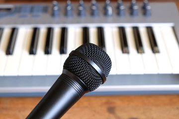 Black vocal microphone close up against defocus electronic synthesizer keyboard with many control knobs in silver plastic body as background