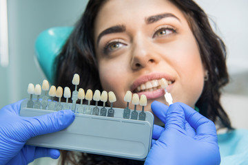 Hand holding tooth color chart. Face of dental patient. Teeth whitening at low price.