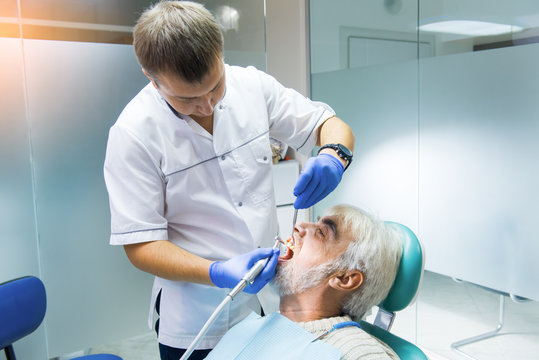 Dentist Cleaning Teeth Of Patient. Old Male In Dental Chair. Oral Hygiene Maintenance.