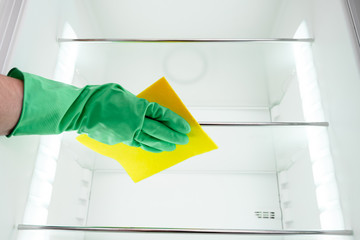 Man's hand in green glove cleaning empty refrigerator