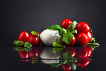 Mozzarella cheese with basil and tomatoes on black table