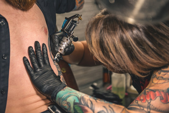 Woman creating tattoo on body of client