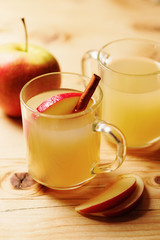 Homemade apple cider in a glass cup with cinnamon and an apple slice on wooden table
