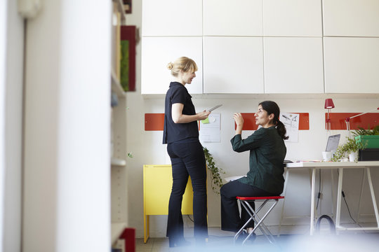 Full length of mid adult businesswoman talking with colleague in office