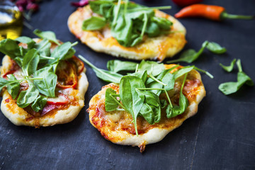 Mini pizzas or bruschettas with cheese, salami and fresh baby spinach leaves.Italian appetizers