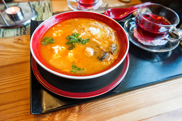 Asian cuisine - Tom kha kai or Thai coconut soup with chicken meat, rice, mushrooms, ginger and lemongrass in red bowl. Close up.