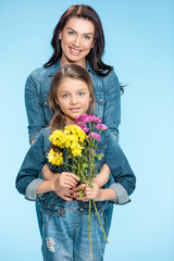 happy mother and daughter hugging and holding flowers in studio on blue, Happy mothers day