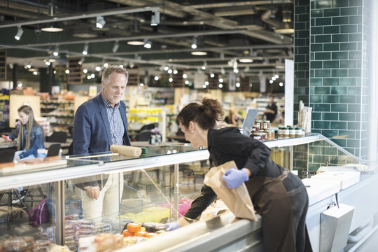 Saleswoman selling food to mature man in organic supermarket