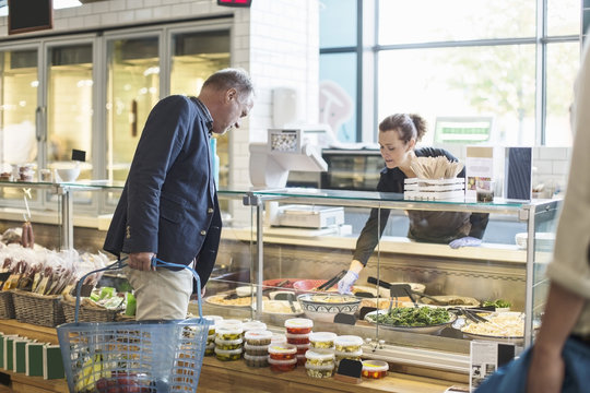 Saleswoman assisting mature man in buying groceries at supermarket