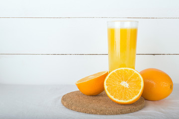 Fresh oranges juice in glass and cork board on white wooden background. Selective focus. Wellness setting. Health concept.