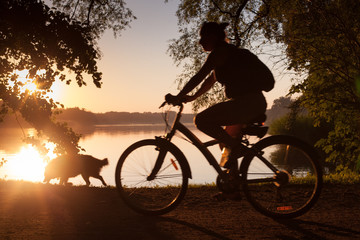 Fototapeta na wymiar Woman cycling on sunset background in park, by the lake.