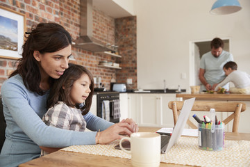 Busy Family Home With Mother Working As Father Prepares Meal