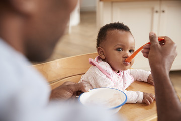 Father Feeding Baby Daughter In High Chair