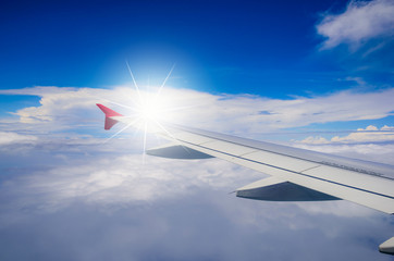 Fototapeta premium Wing of airplane flying above the clouds in the blue sky background.