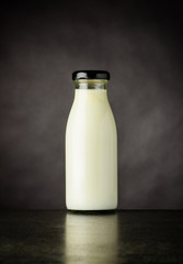 Small Glass Bottle with Milk on Dark Background